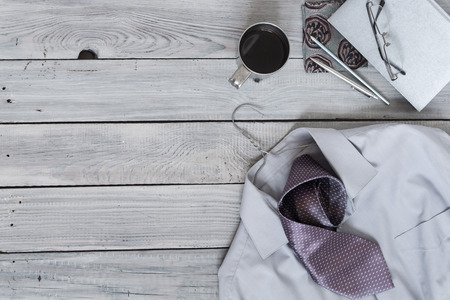 Fragment of a men's shirt with a tie on a hanger, diary, coffee cup on a wooden painted surface. The pastel colorsの写真素材