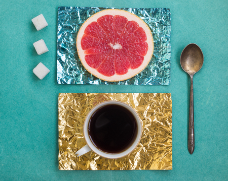 Orange slice and a cup of coffee on stands made of yellow and turquoise foil on a wooden surfaceの写真素材