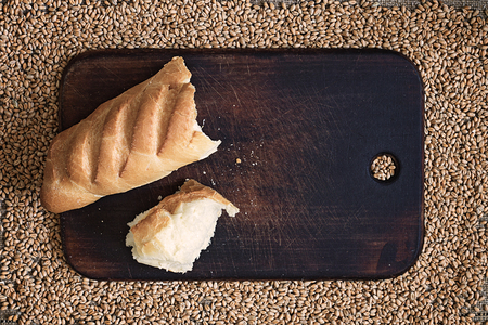 Broken bread on a kitchen board against the background of wheat grainsの写真素材
