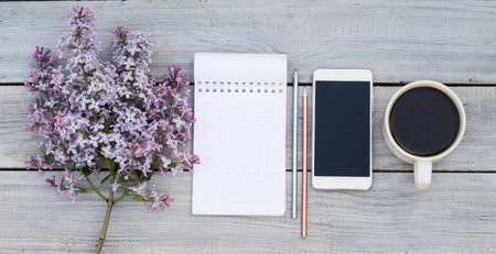 Cup of coffee, notepad, phone and a lilac branch on the white wooden tableの写真素材