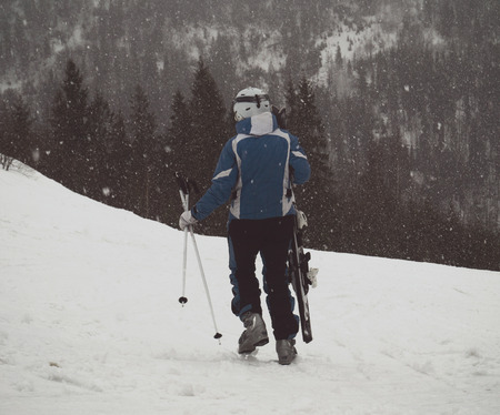 A skier walks down the slope with skis in his hand in the snowの写真素材