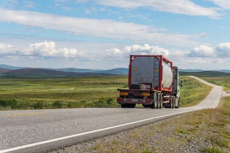 Large tanker truck on the road on a background of green meadow and clouds