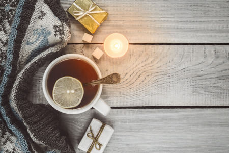 A cup of tea, a knitted scarf and gifts on the background of white wooden tableの写真素材