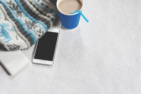 Coffee in paper cups, knitted scarf and phone on a white table. In blue tones
