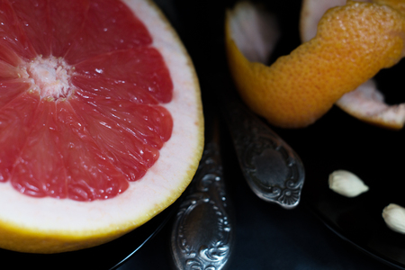 A cut pink grapefruit with a knife and a spoon on dark surfaceの写真素材