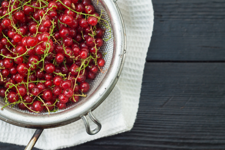 Red currant in a colander on a black wooden tableの写真素材