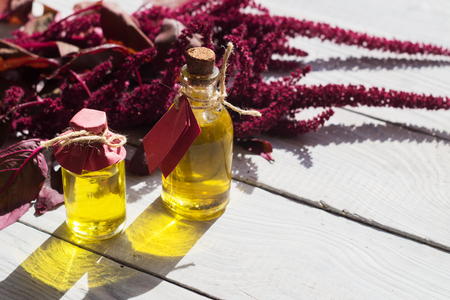 Bottles with amaranth oil and plants of amaranth on a white wooden surfaceの写真素材