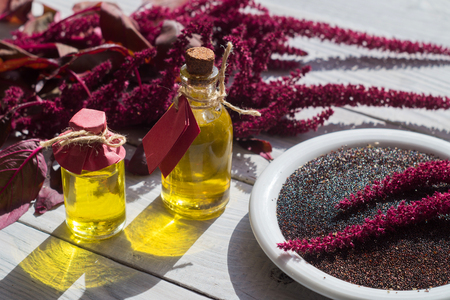 Bottles with amaranth oil, plants and amaranth seeds on a white wooden surfaceの写真素材
