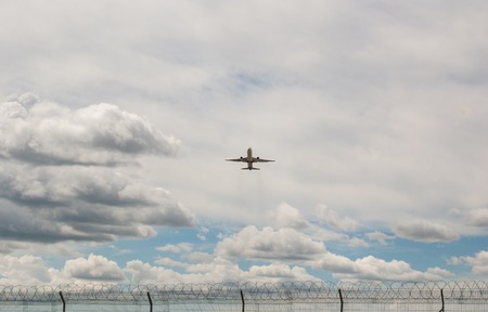 Airplane in the cloudy sky above the metal grid fence