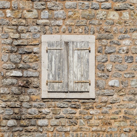 Old window closed with wooden shutters in the stone wallの写真素材