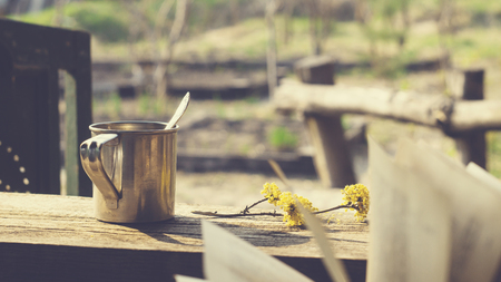 Metal mug, flowering branch and a book on a wooden table in the gardenの写真素材