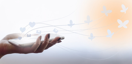 Female hand is holding a phone. Drawn pictures of letters and hearts turn into butterflies. Collageの写真素材