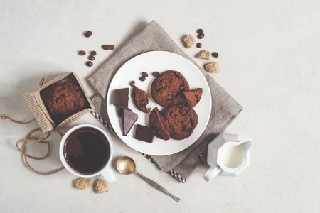 Oatmeal cookies with cocoa and chocolate on a white plate and in a cardboard box, a cup of coffee and a milk jug