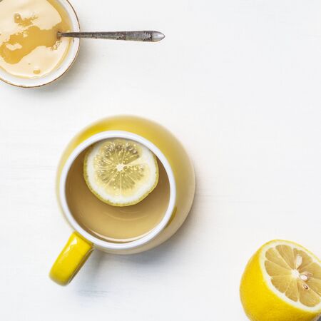 Lemon tea in a yellow cup, honey and half a lemon on a white backgroundの写真素材