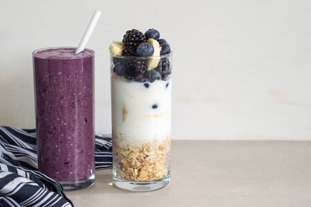 Smoothies of banana, blueberry, blackberry, oatmeal and yogurt and ingredients in two glasses on a light background. Healthy breakfastの写真素材