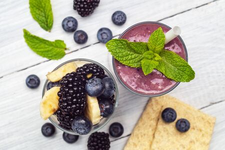Smoothies of banana, blueberry, blackberry, oatmeal and yogurt and ingredients in two glasses on a white table. Top viewの写真素材