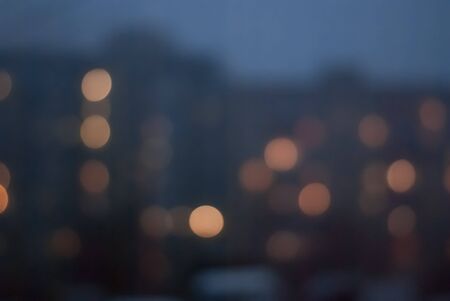 Blurred background of evening cityscape with luminous windows in houses