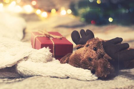 Gift box and toy deer on the background of a Christmas tree with luminous lightsの写真素材
