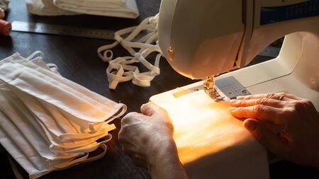 Sewing protective antivirus masks at home. Woman sews masks on a sewing machine