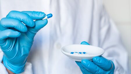 The doctor or pharmacist in blue gloves holding capsules in her handsの写真素材