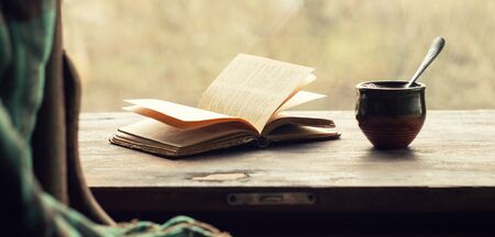 Cup of coffee and an open old book on a wooden windowsill. Retro styleの写真素材