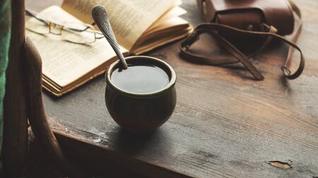 Cup of coffee, old book and glasses on the windowsill, near a chair with a plaid. Retro styleの写真素材