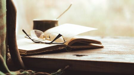 Cup of coffee, old book and glasses on the windowsill, near a chair with a plaid. Retro styleの写真素材
