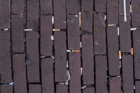 Paving stones on the street with many cigarette butts and plastic trash. Top view
