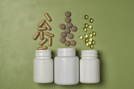 Multi-colored pills and capsules with vitamins or dietary supplements fly out of three white plastic jarsの写真素材