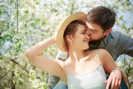 Radiant couple kissing in the blooming park. Young husband kisses beautiful wifeの写真素材