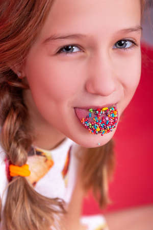 Closeup smiling portrait of teenage girl show tongue out with small edible rainbow colored balls for topping cake easterの写真素材