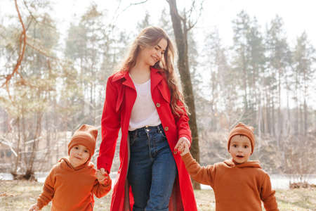 Happy young beautiful mother holds two little sons by the hands. Weekend walk in the spring forest. Children boys twinsの写真素材