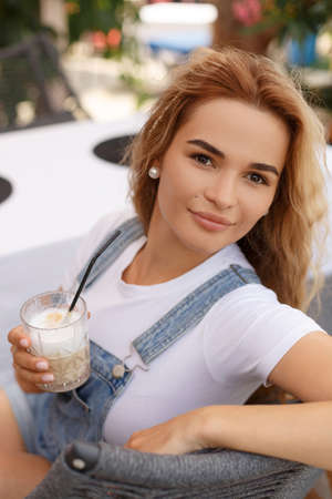 White blonde woman holding a glass of coffee latte in her hand. Portrait of a beautiful young adult...