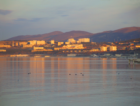 The sea landscape with houses illuminated by the rays of the setting sun against the backdrop of the mountainsの写真素材