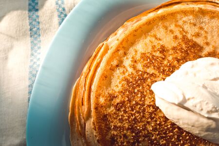 pancakes with sour cream are stacked on top of each other on a blue plateの写真素材