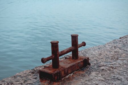 Rusty steel double berth on a fragment of an old concrete pier against a background of turquoise sea waterの写真素材