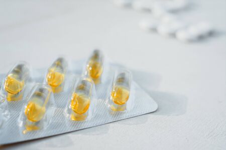 a lot of white round tablets and a few yellow capsules lying on a white background. the view from...