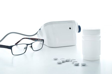 white pills scattered from plastic jar in front of blood pressure monitor, toned, glasses