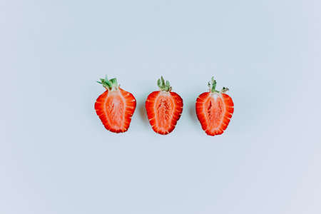 Fresh strawberry slices. A group of three strawberry slices is laid out in a line with green leaves on a blue background. Juicy strawberry slicesの写真素材