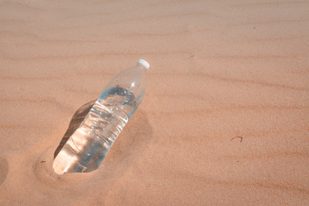 a bottle of water in close-up on the yellow sand, quenching your thirst on a hot summer day. A plastic bottle of cold water left on the sand. in pastel colors. horizontal photoの写真素材