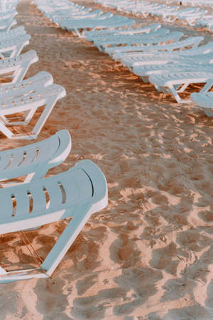 lots of white sun beds on the sandy beach. The image is in pastel colors. Vertical photoの写真素材