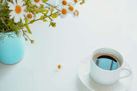 A bouquet of daisies in a blue vase on a white background. A cup of black coffee.The concept of breakfast in nature.の写真素材