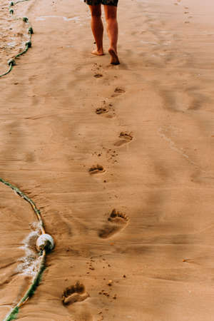 footprints on the yellow sand, in the distance mens feet walking on a sandy beach