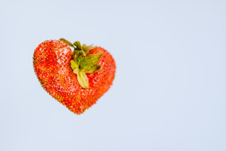 ripe strawberry berry in the shape of a heart. Red berry strawberry heart shape, isolated on a light background. selective focus on the berry. Valentines day greeting conceptの写真素材