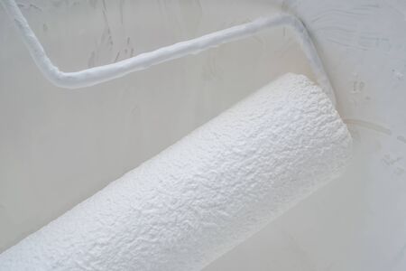 paint background concept, closeup of acrylic oil paint roller with modern white color above abstract rough surface vintage dark grey plaster wall texture for decorating interior design with copy spaceの写真素材