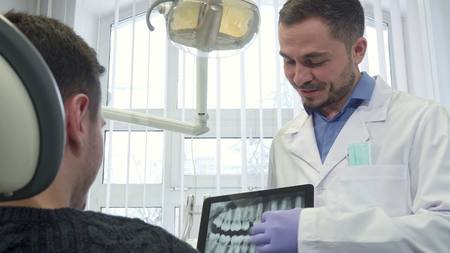 Dentist shows male client x-ray on his tabletの写真素材