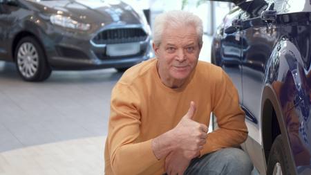 Senior man examines the car wheel at the dealershipの写真素材