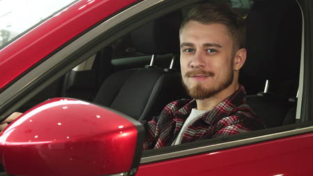 Handsome young man sitting comfortably in his new car smiling to the camera