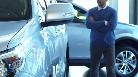 A solid man walks through the automobile showroom and looks at the car