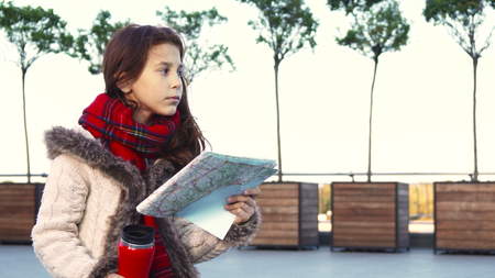 A little girl is studying a map and dreamily staring into the distance